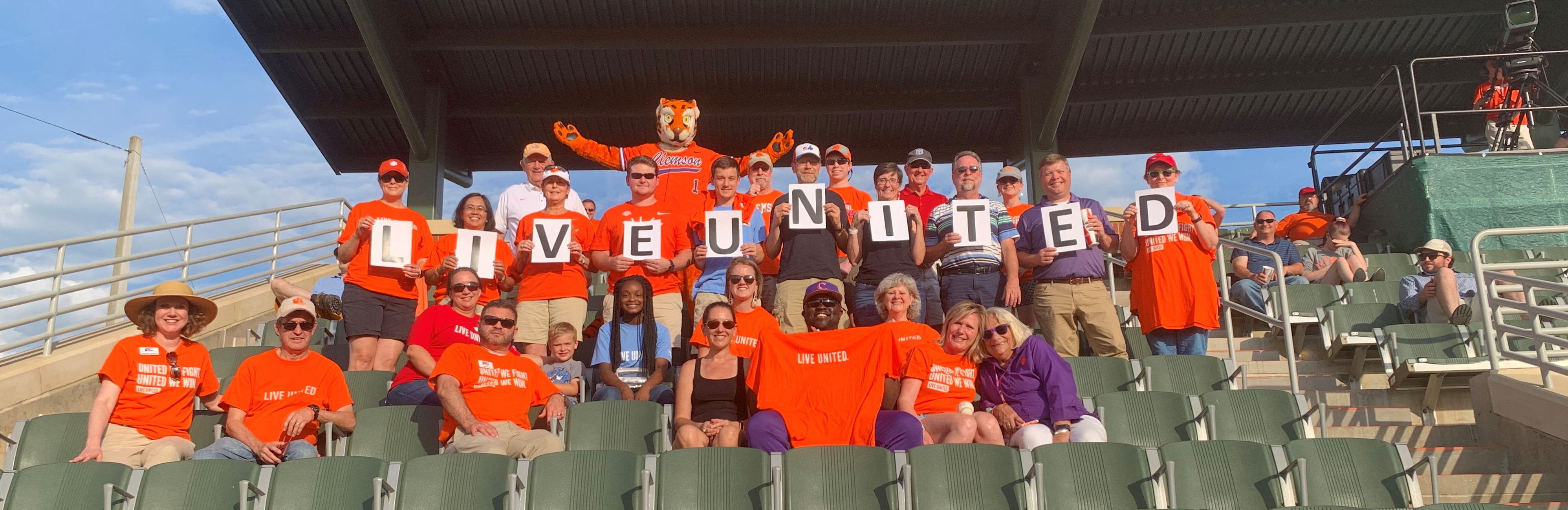 Clemson University employees at baseball game holding Live United sign with Clemson Tiger