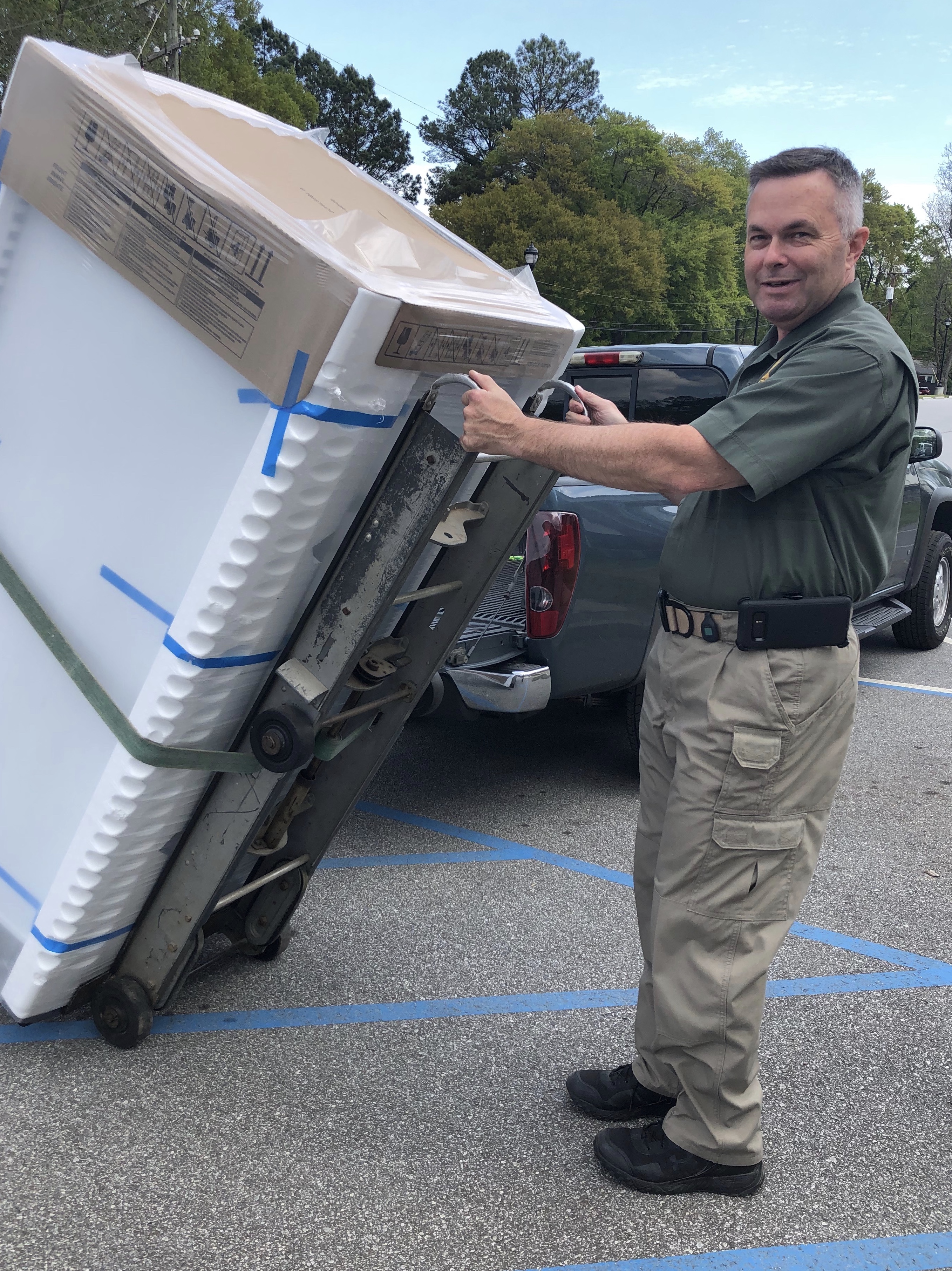 "Sheriff Rick Clark holds a newly purchased freezer on a moving dolly"
