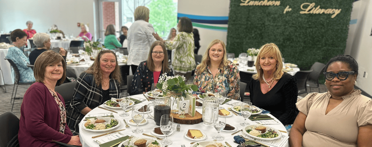 a group of women smile at the camera while seated at their table during the Luncheon for Literacy