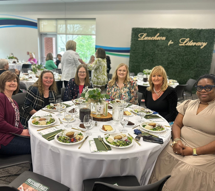 a group of women smile at the camera while seated at their table during the Luncheon for Literacy