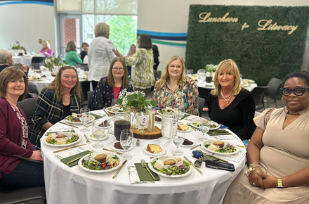 a group of women smile at the camera while seated at their table during the Luncheon for Literacy