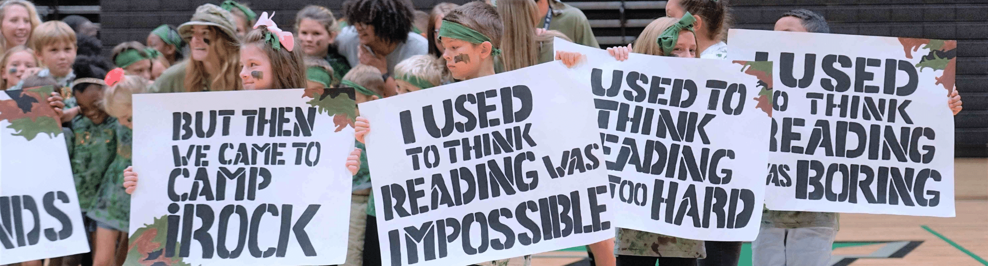 camp irock students hold signs that say i used to think reading was boring, hard and impossible. But then I came to Camp iRock.