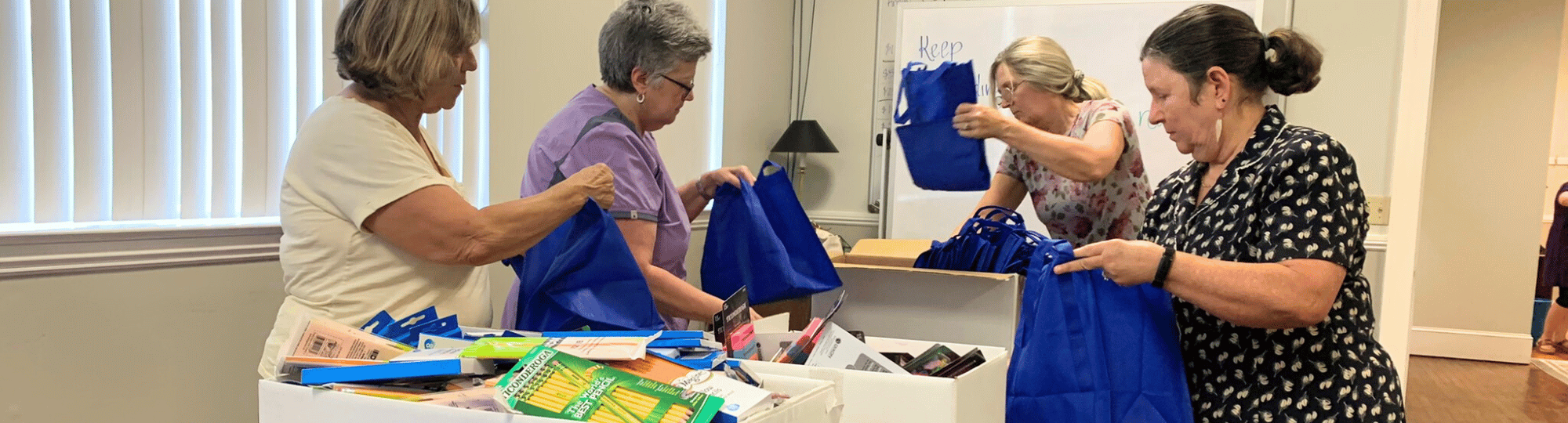 Four women stuffing school supplies into blue bags