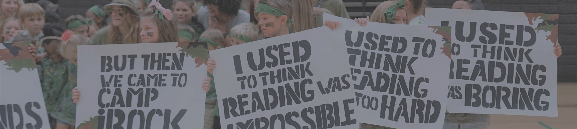 Camp iRock campers hold up signs that say I used to think reading was boring, hard and impossible but then we came to camp irock