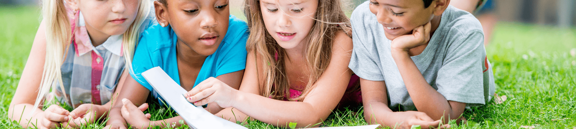four children laying in the grass reading a book together