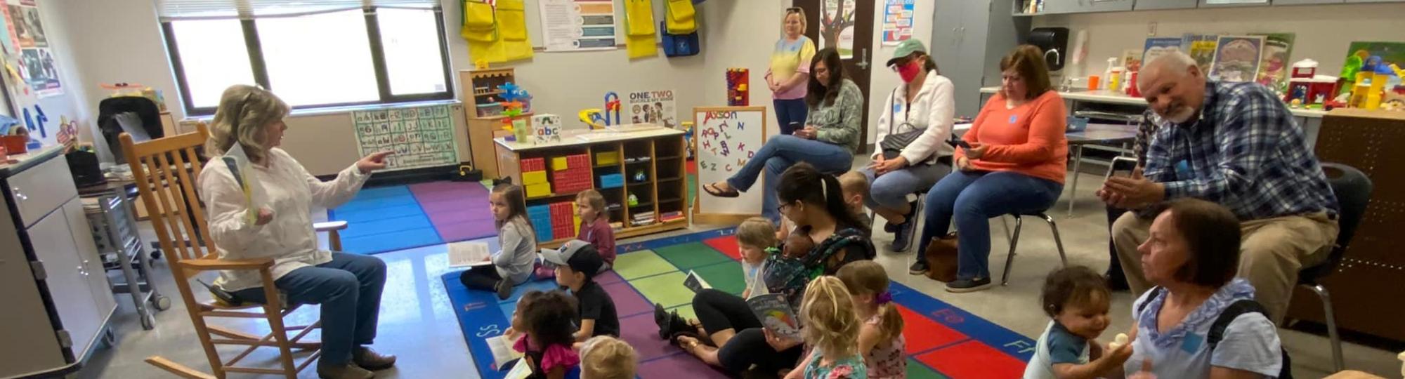 Teacher reading a book to a class of Preschool Pages students and caregivers