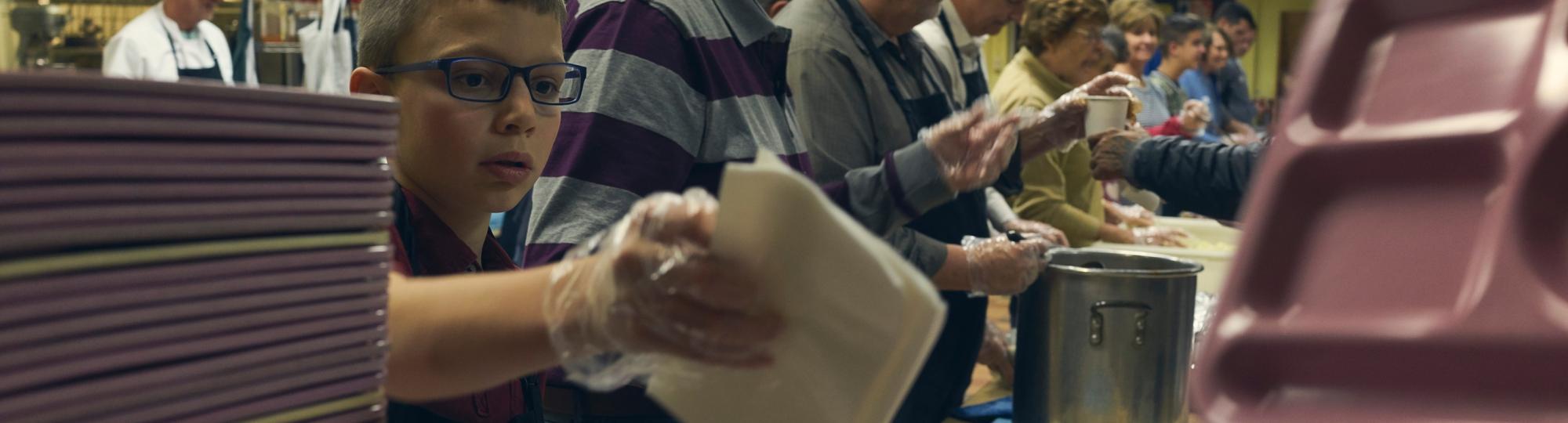 boy and adults volunteer handing out meals at a soup kitchen