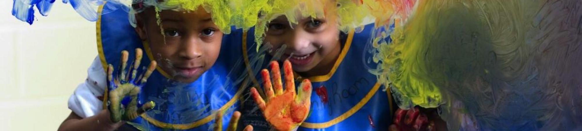 Two children peer through a glass wall where they have been painting with their hands