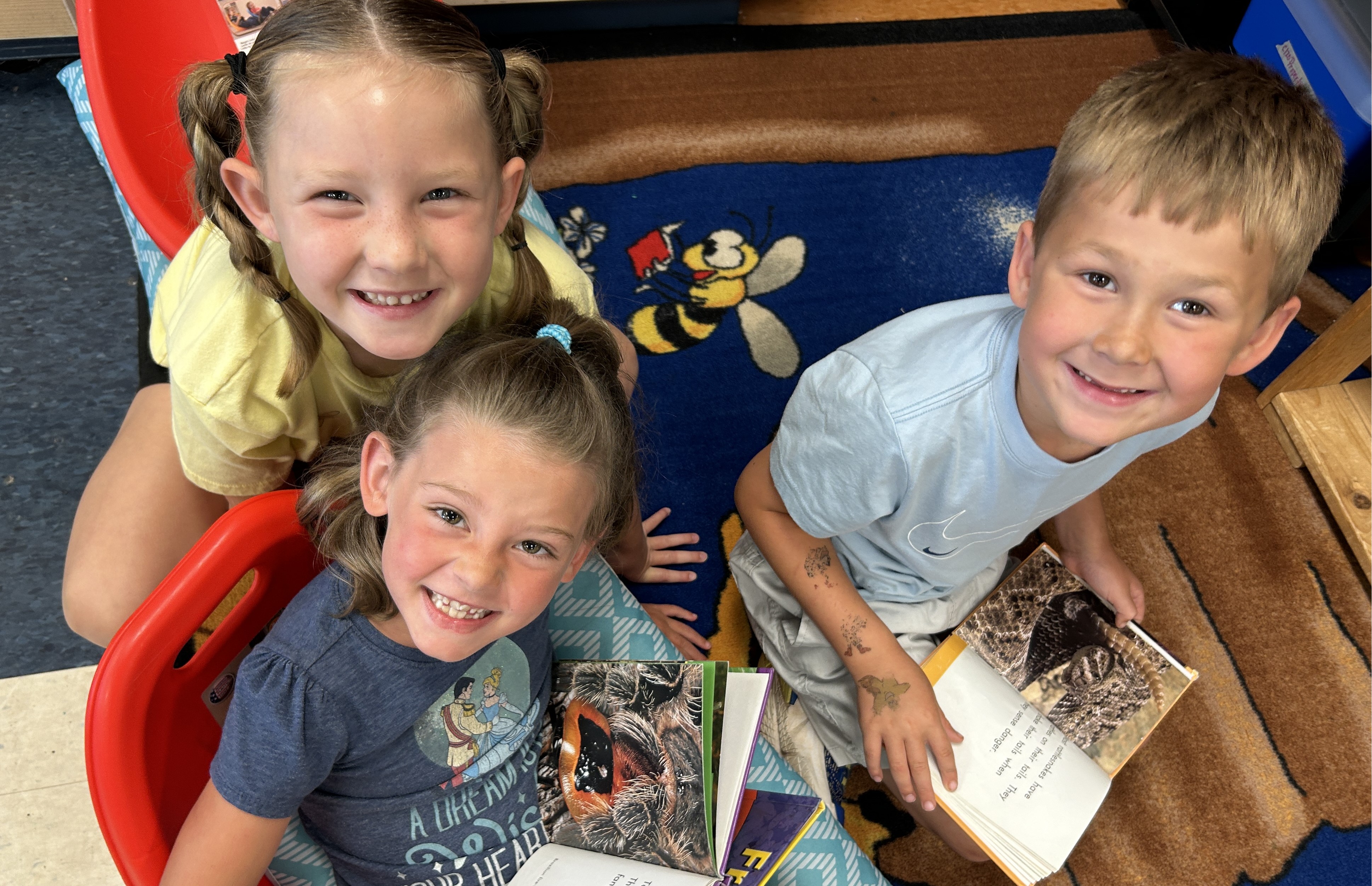 Three children holding books and looking up at the camera at Camp iRock.