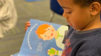 A toddler boy holds a Preschool Pages book