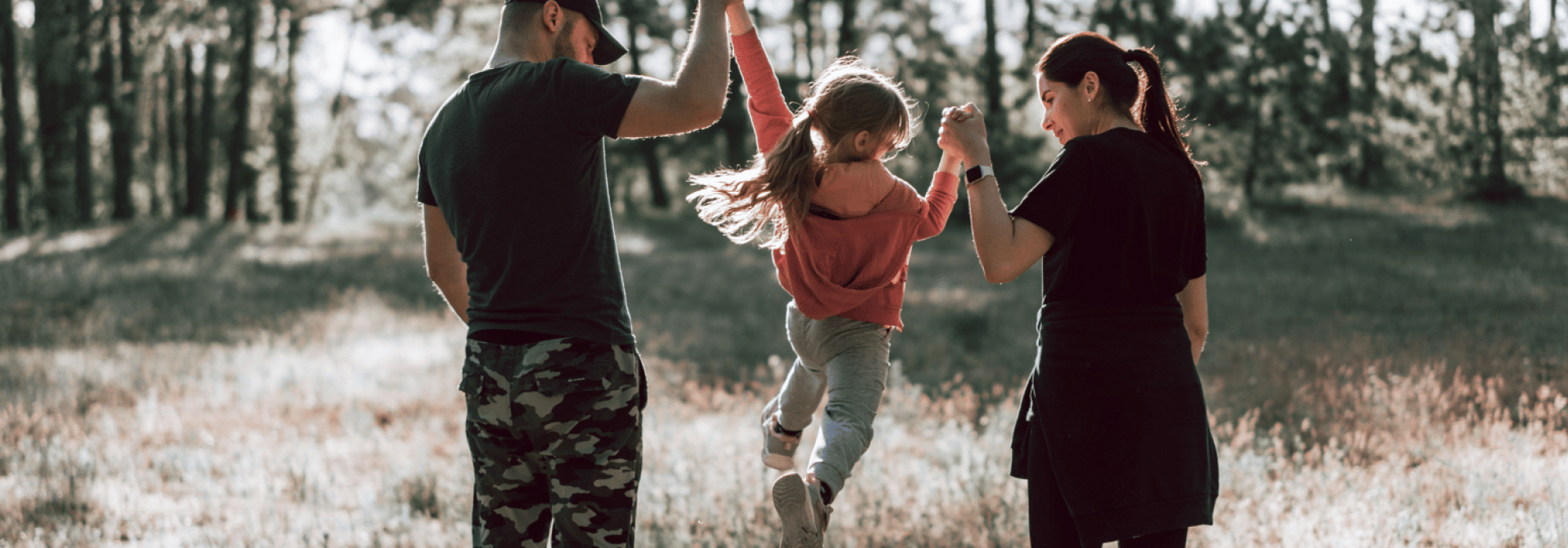 dad and mom lifting daughter in air while walking in a field