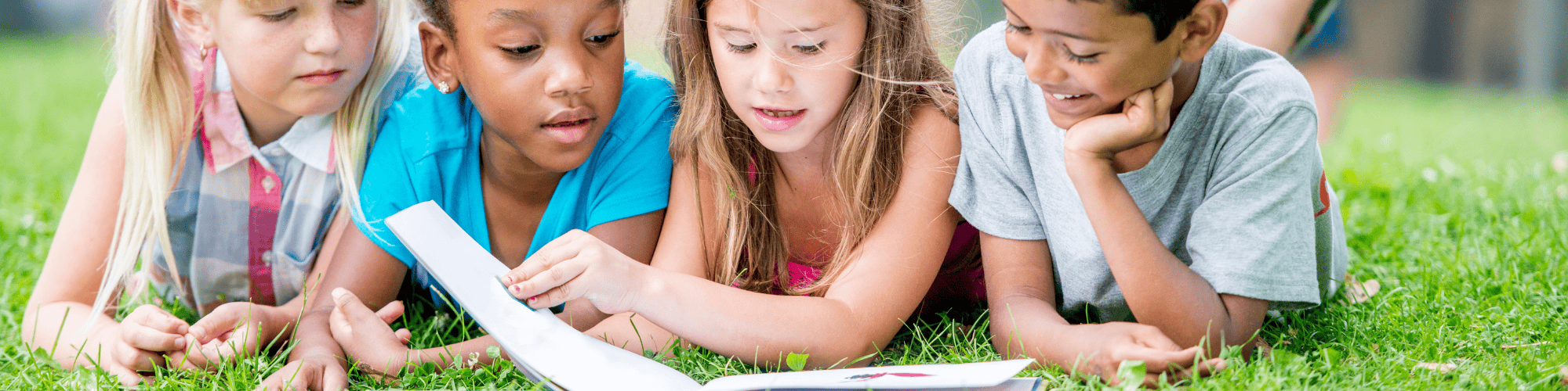 four children laying in the grass reading a book together