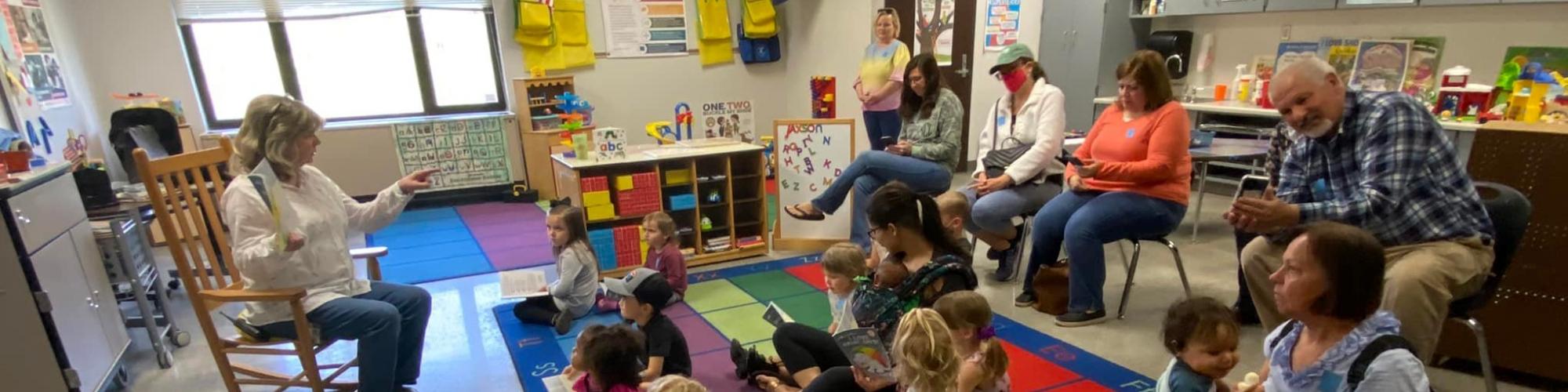 Teacher reading a book to a class of Preschool Pages students and caregivers