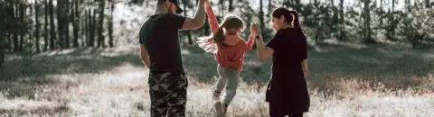dad and mom lifting daughter in air while walking in a field