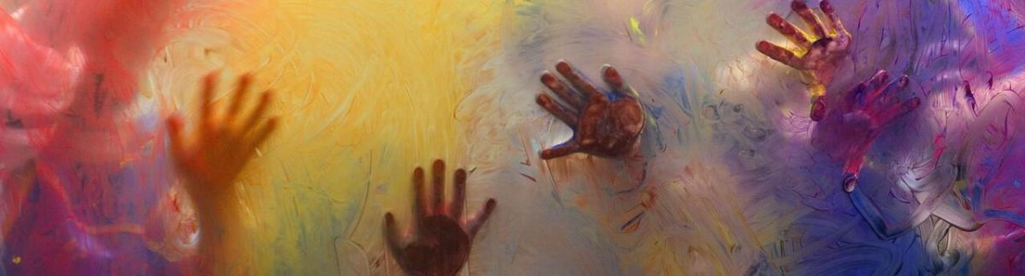 childrens hands held up on a glass wall with colorful paint 